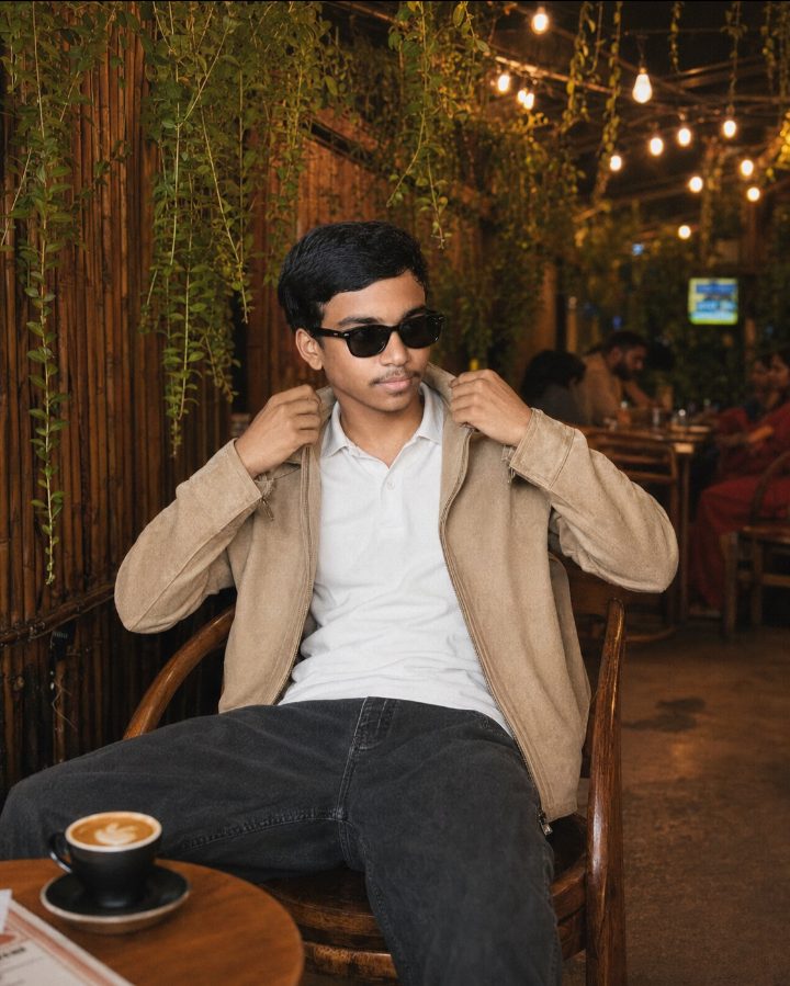 a young man sitting on a wooden chair in an outdoor garden café